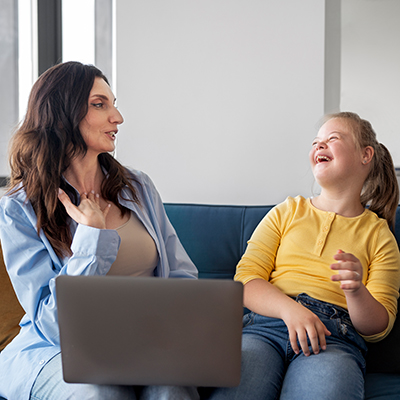 Eine erwachse Frau und ein junges Mädchen mit Downsyndrom sitzen gemeinsam auf einer Couch